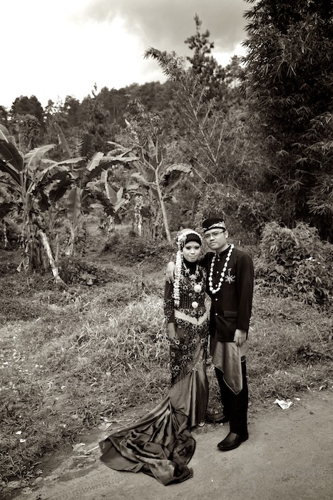 Indonesian bride and groom pose outside by banana trees
